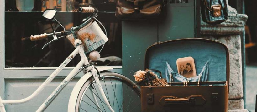 古びた白い自転車と花束の入っている蓋の空いたトランクケース